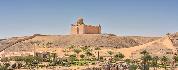An architectural marvel from Egypt atop a desert hill with a lush Nile River view. Nearby palm trees and greenery reflect the unique harmony of desert and river landscapes surrounding the ancient structure.