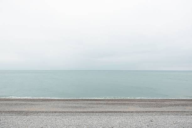 A minimalist seascape featuring calm water and a cloudy sky over a pebble beach
