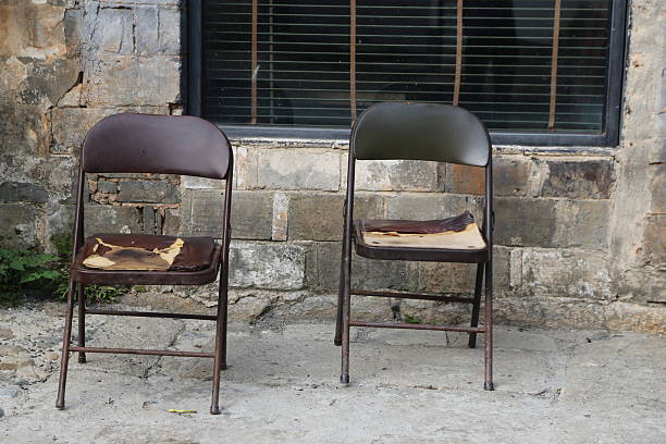 two metal folding chairs with leather seats and backrests, both of them broken in the same spot, held together by a patchwork piece of cloth