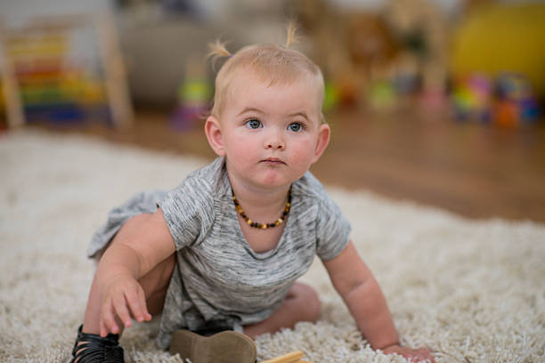 A curious baby crawls on a fluffy rug in a cozy home environment, wearing a grey shirt and amber necklace. Bright, warm lighting creates a welcoming, family-friendly scene.