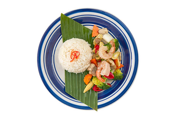 Stir-fried mixed vegetables with shrimp served with steamed rice on banana leaf. Thai cuisine isolated on white background with clipping path, top view.