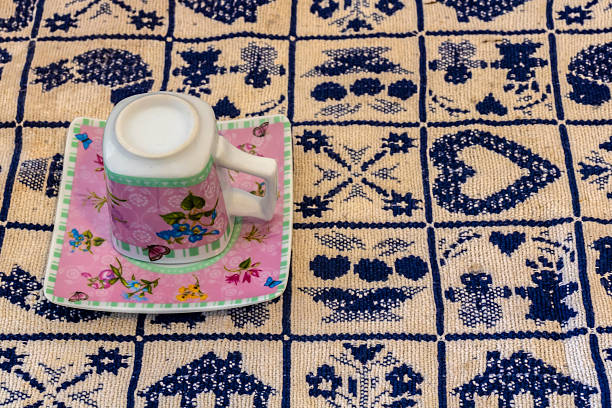 Floral porcelain cup upside down on a square saucer, resting on an embroidered tablecloth with geometric and traditional patterns, symbolizing Brazilian craft and domestic culture.