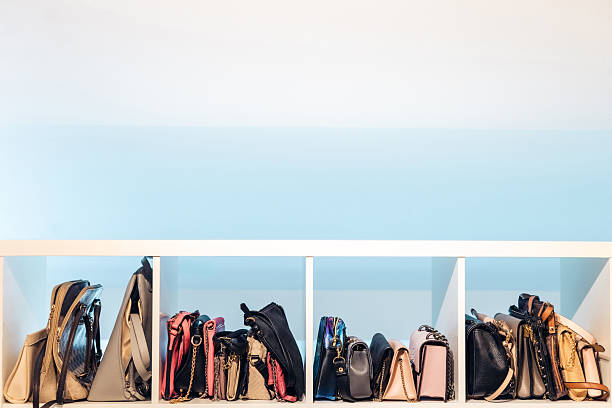 Organized row of assorted handbags displayed in white cubby shelf against clean pastel wall