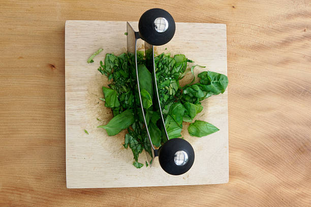 A double mezzaluna kife or rocking knife is used to finely cut basil in preparation for making pesto