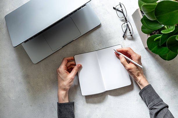 istock Hands writing in notebook near headset and laptop, top view. Customer support equipment at call center. Online conference. Online education concept 2243718884