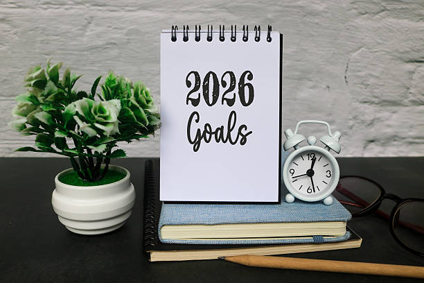 istock Hand Writing 2026 Goals on Notebook with a clock, glasses, and planner on the desk. New year planning, motivation, productivity, and goal setting for 2026. 2243722766