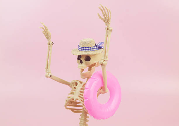 Human skeleton in hat with inflatable swim ring on pink background. Funny Halloween concept.