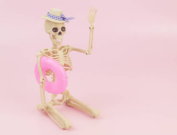 Human skeleton in hat with inflatable swim ring on pink background. Funny Halloween concept.