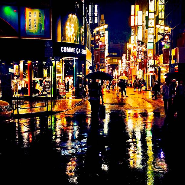 Captured on a rainy night in the heart of Tokyo, this vibrant street scene reflects the dazzling glow of neon signs on the wet pavement. Locals walk under umbrellas, weaving through a colorful cityscape of lights, reflections, and motion. The contrast between shadow and illumination turns an ordinary evening into a cinematic moment full of urban poetry.Editorial use only – real location, unaltered shopfronts and signage.