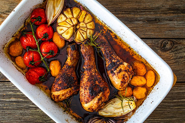Stock photo showing close-up, elevated view of  a traditional roast chicken dinner served for Sunday lunch on an oval, green serving plate, featuring juicy roasted chicken, golden potatoes, pigs in blankets (pork cocktail sausages wrapped in bacon), sliced carrot and tender Brussels sprouts. This stock image highlights hearty home-cooked meals, comfort food, and family dining.