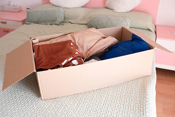 istock Cardboard box filled with assorted clothing items sits on a neatly made bed, showcasing a cozy bedroom environment with soft textures and pastel colors 2243730964