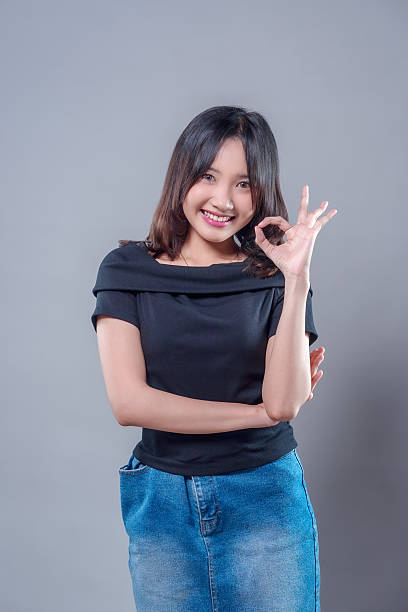 istock A young Asian woman smiling confidently while showing an OK hand gesture, symbolizing positivity and approval, dressed casually in a black top and denim skirt with a cheerful and friendly expression. 2243735199