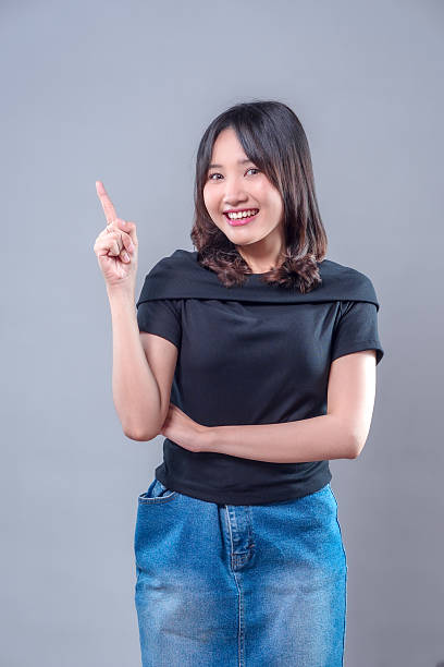 istock A cheerful Asian woman smiling brightly while pointing upward with one finger, expressing a positive idea and confidence in a casual outfit, representing creativity and optimism. 2243735279