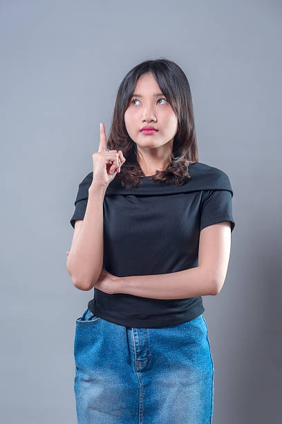 istock A young Asian woman looking thoughtful while pointing upward with one finger, expressing a moment of realization or new idea, dressed casually in a black shirt and denim skirt with a focused expression. 2243735280