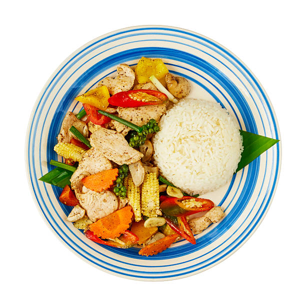 Thai spicy stir-fried pork with vegetables, peppercorn, and rice on blue-striped plate. Isolated on white background with clipping path, top view.