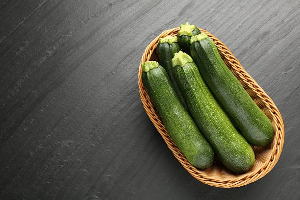istock Fresh ripe zucchinis in wicker basket on black table, top view. Space for text 2243736048