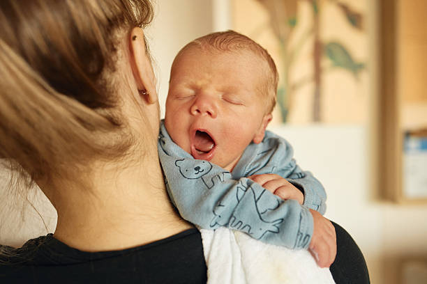 Mother holding newborn baby yawning after feed stock photo