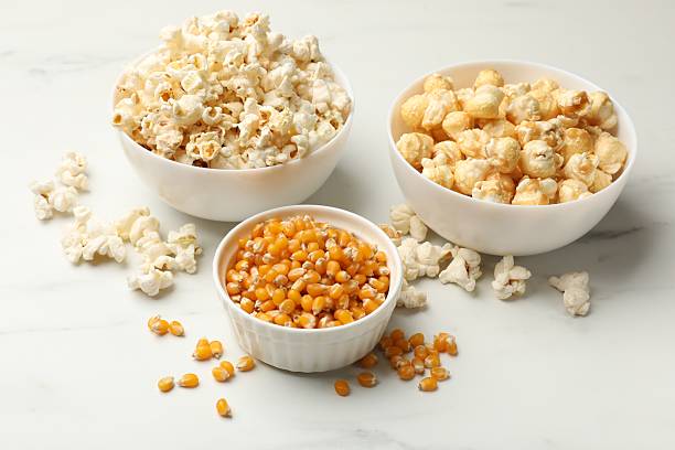 istock Tasty popcorn and corn kernels on white table, closeup 2243739011