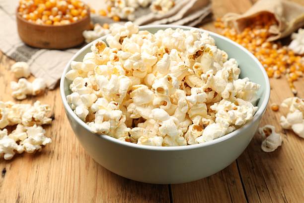 istock Tasty popcorn and corn kernels on wooden table, closeup 2243739032