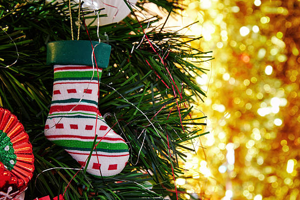 A festive Christmas stocking ornament hangs on a decorated tree with soft, golden bokeh lights in the background