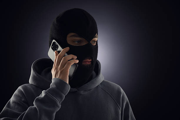 istock Criminal in mask talking on phone against dark background. Space for text 2243743559