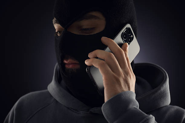 istock Criminal in mask talking on phone against dark background 2243743655