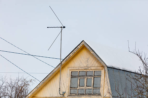 A house with a roof and a window. The window is covered with snow. There is a satellite dish on the roof