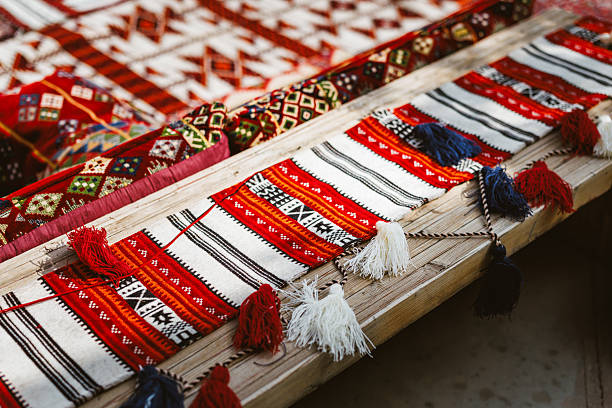 Close up shot featuring vibrant textiles and intricate patterns on wooden seating in a traditional Middle Eastern outdoor majlis. Red, white, and black designs with decorative tassels create a colorful and inviting atmosphere.