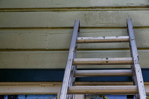 a worker climbing up on construction aluminium ladder placed outside of the house, in black and white
