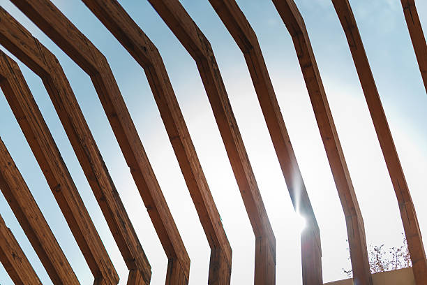 Close up shot featuring wooden slatted roof structure in Arabic architecture with bright sky visible through the gaps. Sunlight filters through wooden beams, highlighting the intricate design and craftsmanship typical of traditional Arabic architectural elements.