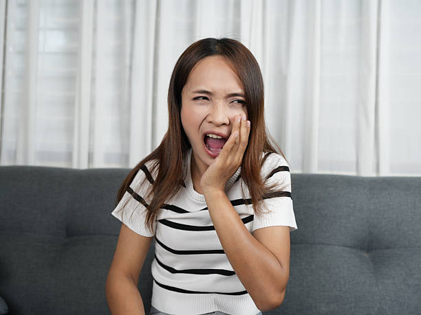istock Woman sitting on couch expresses discomfort while holding her face, possibly due to toothache. Her facial expression conveys pain and frustration, highlighting emotional impact of dental issues 2243748010