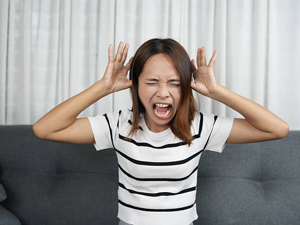 istock Frustrated woman expressing anger while sitting on couch, covering her ears with her hands. scene captures moment of emotional distress in cozy indoor setting 2243748049