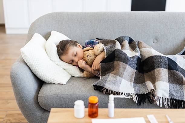 istock Sick child sleeping on a couch with a teddy bear 2243748870