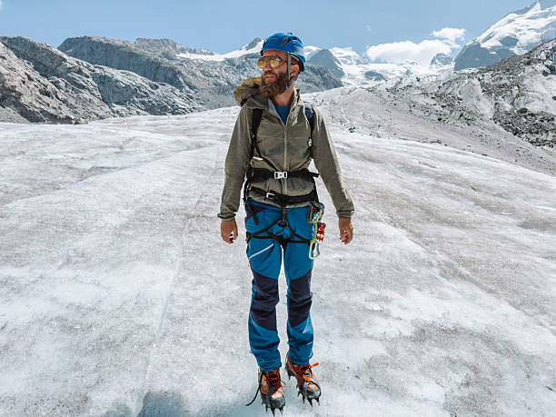 Bearded man wearing helmet and crampons hiking on icy glacier terrain. Outdoor adventure on snowy mountain with climbing equipment. Mountaineer exploring rugged alpine environment.