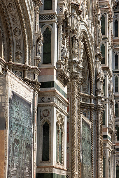 Close up shot featuring the intricate marble facade of Florence Cathedral, highlighting detailed stone carvings and architectural features. The sunlight enhances the relief and shadow effects on the ornate exterior. This historic structure showcases exemplary craftsmanship and design.