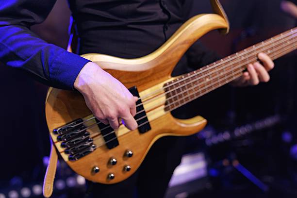 Close-up of a musician's hand actively plucking the strings of a five-string wooden electric bass guitar during a live music performance.