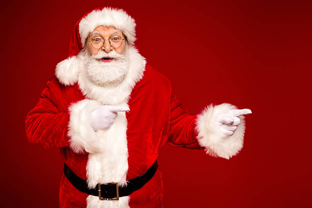 istock Santa Claus in red suit with white fur points playfully against a bold red background for a festive holiday season image 2243757704