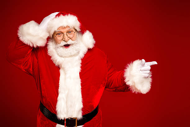 istock Santa Claus in a bright red costume smiles and points against a solid red background perfect for Christmas holidays family celebration 2243757707