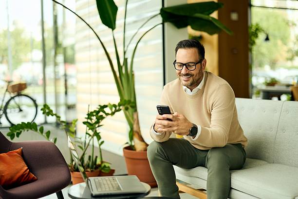 istock Businessman Smiling While Using Smartphone in Modern Office Lounge With Green Plants 2243757969