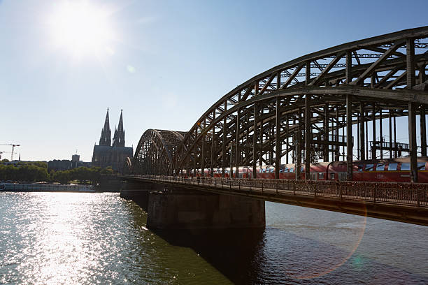 Cologne, Germany - August 11, 2025:people walking on Hoherzollern bridge over river Rhine in Cologne, Germany at a hot summer day while a train is passing by, view to the cathedral