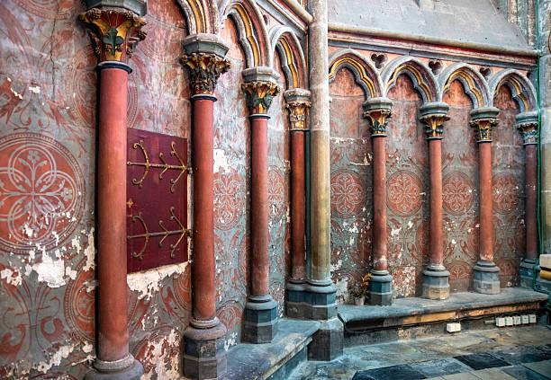 church the notre dame in amiens interior featuring tall blue-green columns with golden capitals, arched arches, and faded wall murals. A colorful stained glass window