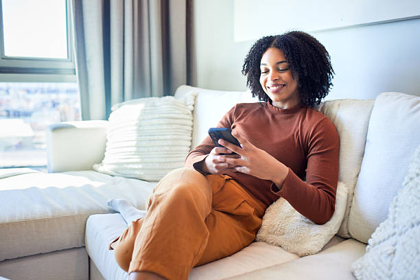 istock Happy Black Woman Smiling While Texting on Sofa at Home 2243763318