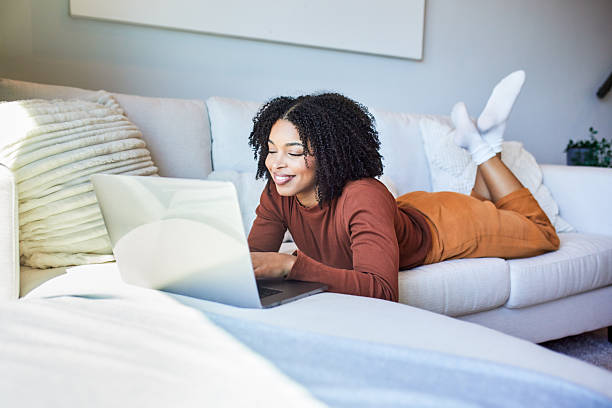 istock Happy Black Woman Smiling While Working on Laptop Lying on Sofa 2243763411