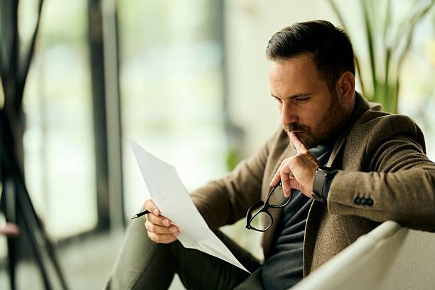 Thoughtful Businessman Reviewing Documents with Glasses in a Modern Office Setting