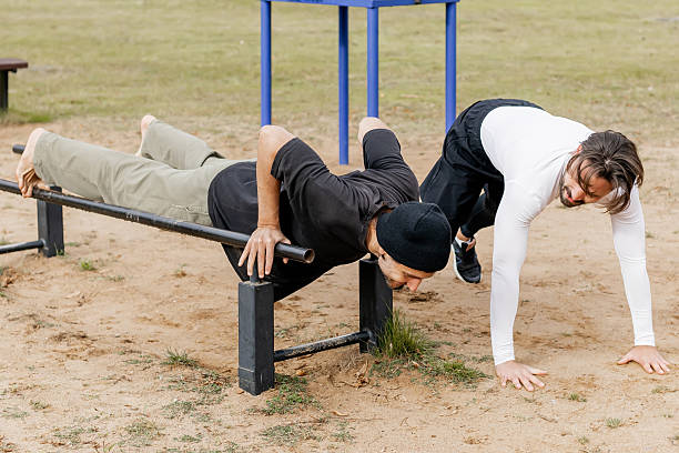 istock Two young men exercising outdoors on parallel bars in a park, one performing a push-up on the bars while the other watches and encourages, showcasing friendship, fitness, and outdoor training in a natural setting 2243769685