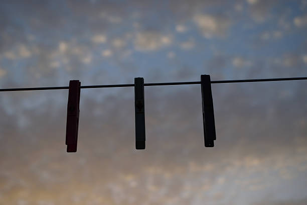 image shows four clothespins hanging on a clothesline with a soft, cloudy sky in the background. The photo is composed with the line stretching diagonally across the frame, and the clothespins spaced evenly along it, creating a simple, colorful, and slightly nostalgic outdoor scene. clothespins, clothesline, blue, red, green, black, outdoor, cloudy sky, simplicity, colorful, everyday objects, minimalist composition.