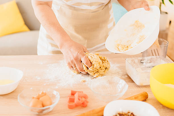 A woman is kneading dough for bread and cakes and adds flour.