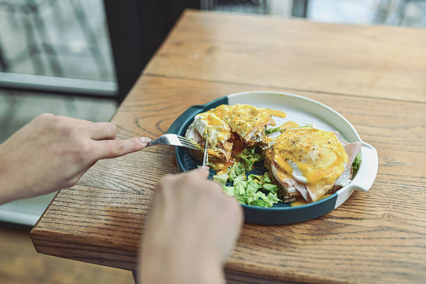 Served on a white plate, two open-faced sandwiches topped with melted cheese and greens. A person plates breakfast in a relaxed, contemporary lounge bar, suggesting warmth and social dining.