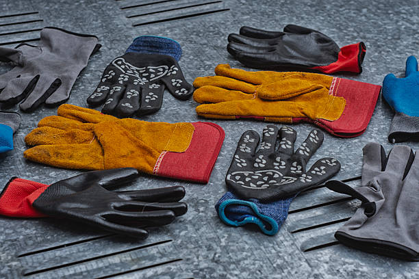 Set of various protective work gloves in different colors and materials placed on a metallic textured surface. Concept of safety equipment, industrial protection, and construction accessories