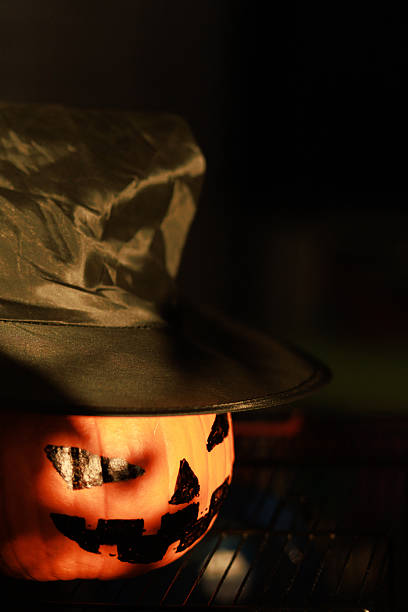 Close up of Halloween pumpkin wearing witch hat in dark dramatic light.Concept of spooky season, mystery and creative holiday design.